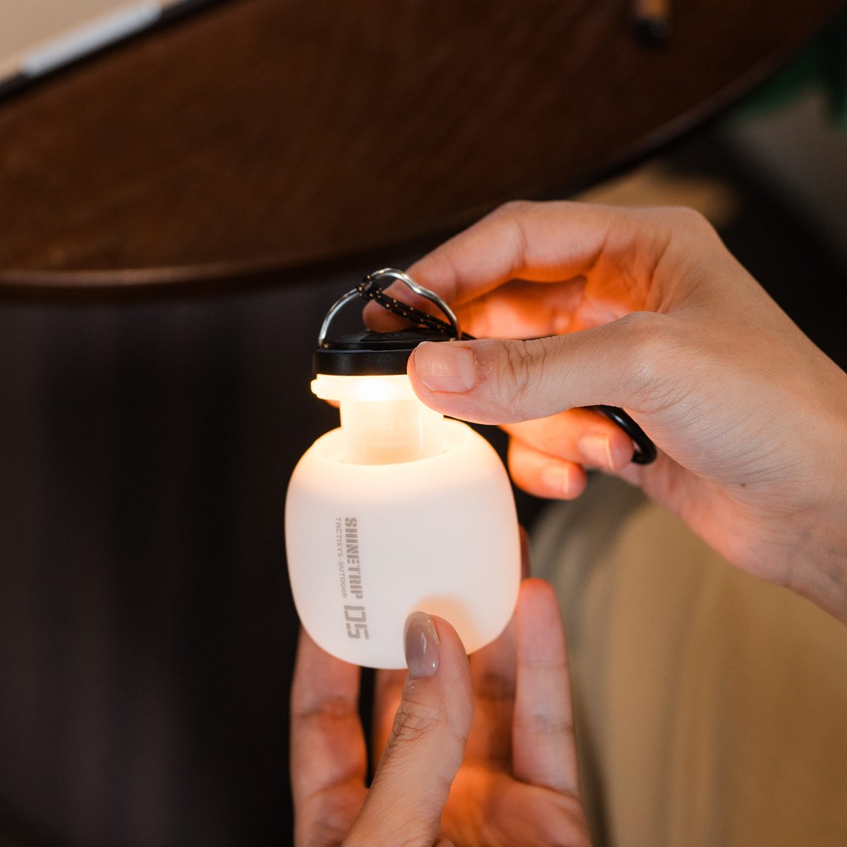 A hand holding the A61 Acorn Lamp with the silicone shade removed, showing the glowing diffuser and the metal clip on the top cap