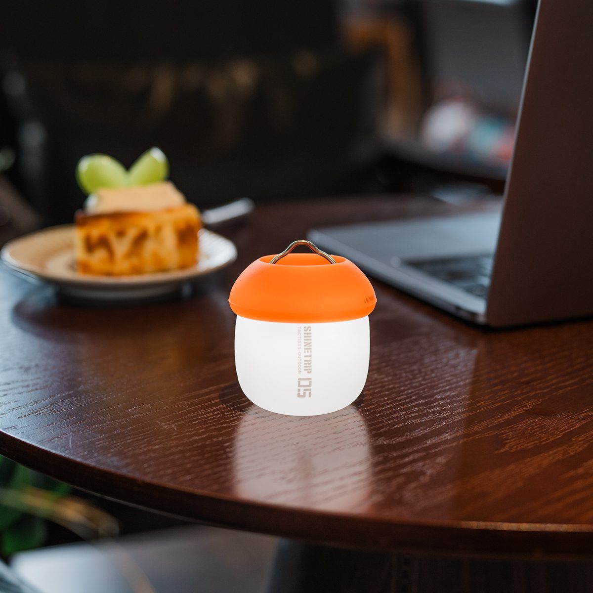 A61 Acorn Lamp with the orange silicone shade fitted, glowing on a cafe table