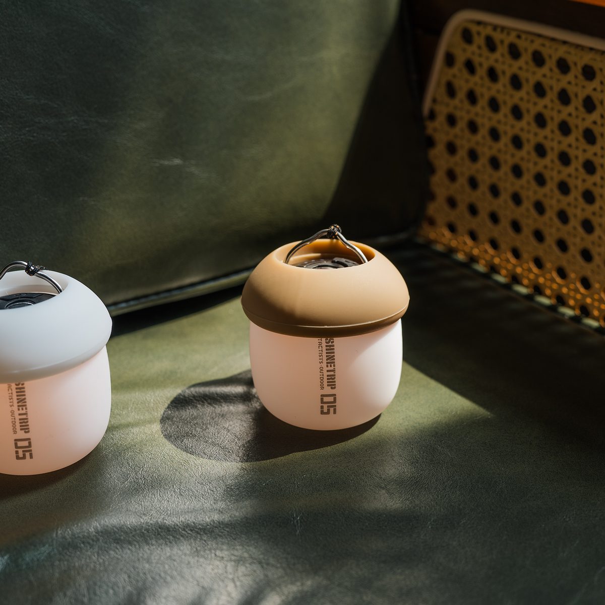Two A61 Acorn Lamps, one with a white shade and one with a sand shade, resting on a green leather chair